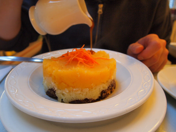 A full serving of haggis, neeps and tatties on a white plate, with gravy being poured