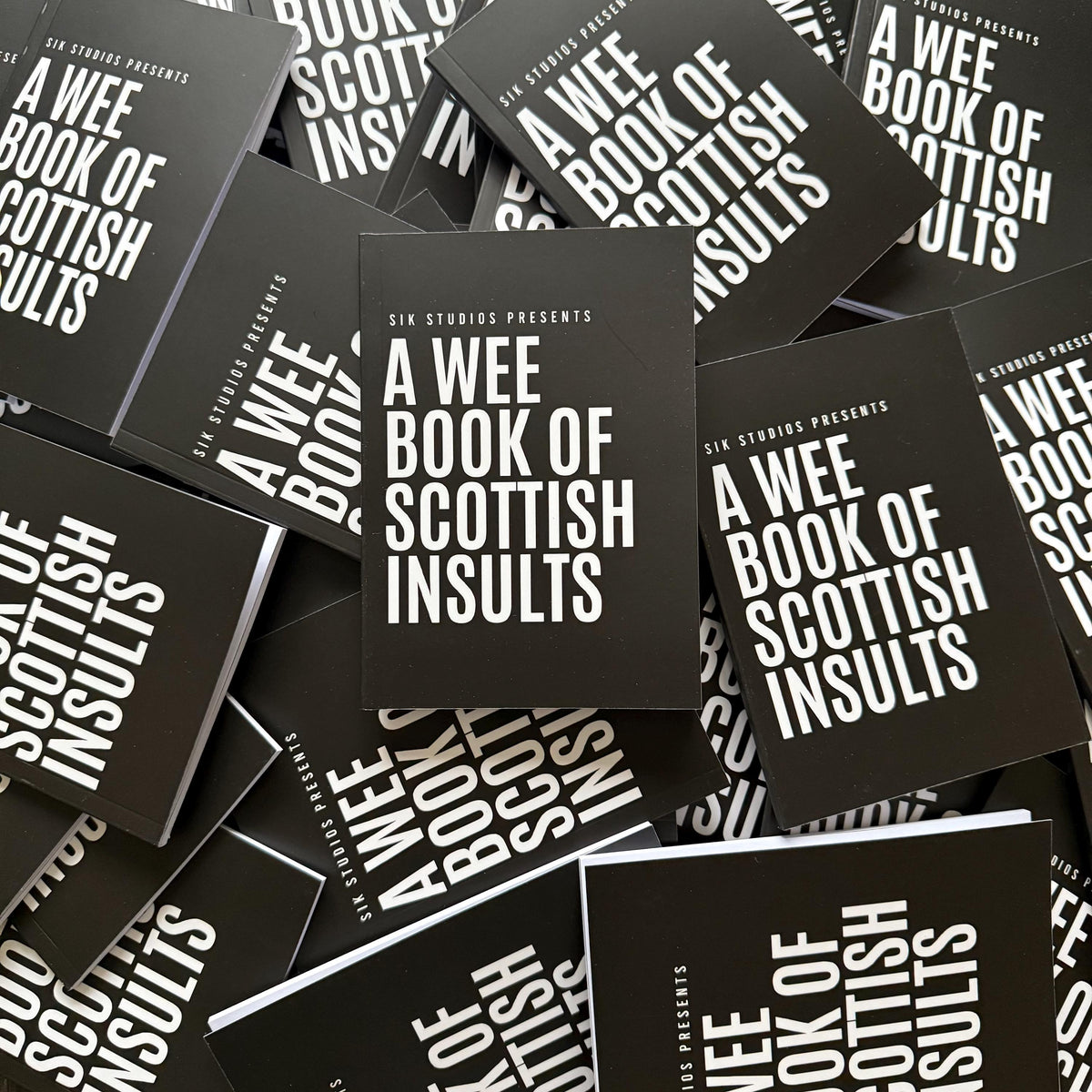 A Wee Book of Scottish Insults — a scattered pile of copies of the black paperback